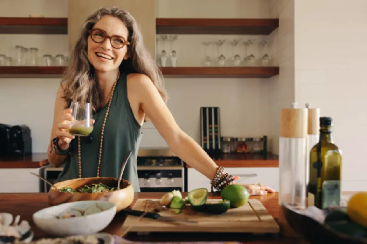 Healthy woman smiling while holding green juice in her kitchen.